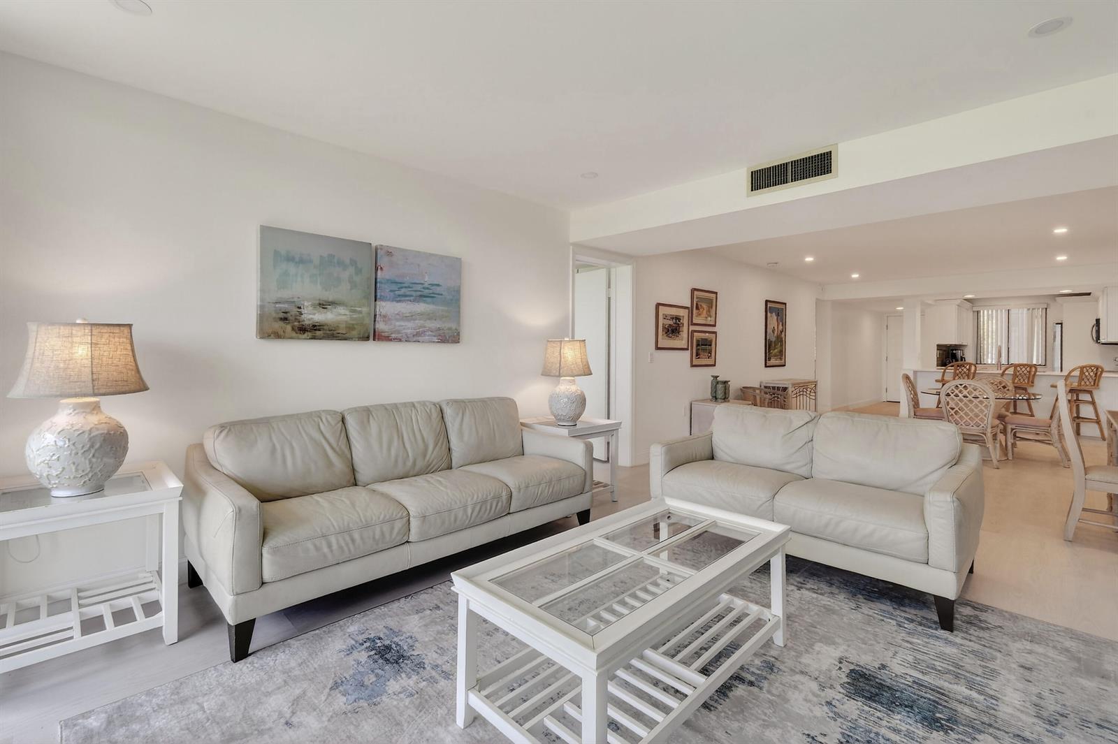 A living room features two light-colored leather sofas, a glass-topped coffee table, and area rug — 301 S Seas Drive # 104, Jupiter FL 33477, JUPITER, FL