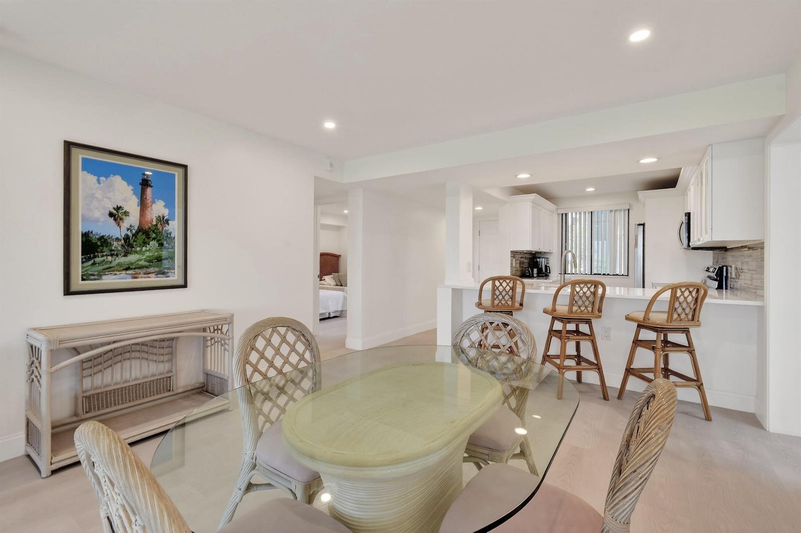 A dining area with a glass table and rattan chairs sits adjacent to a white kitchen — 301 S Seas Drive # 104, Jupiter FL 33477, JUPITER, FL