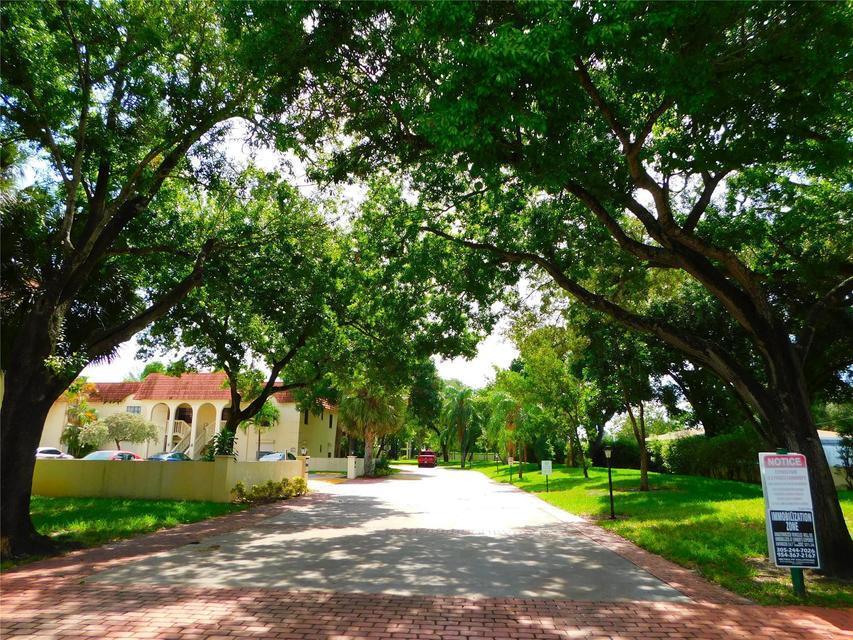 A paved driveway leads toward a multi-story apartment building shaded by large, mature trees — 134 S Cypress Road # 425, Pompano Beach FL 33060, POMPANO BEACH, FL