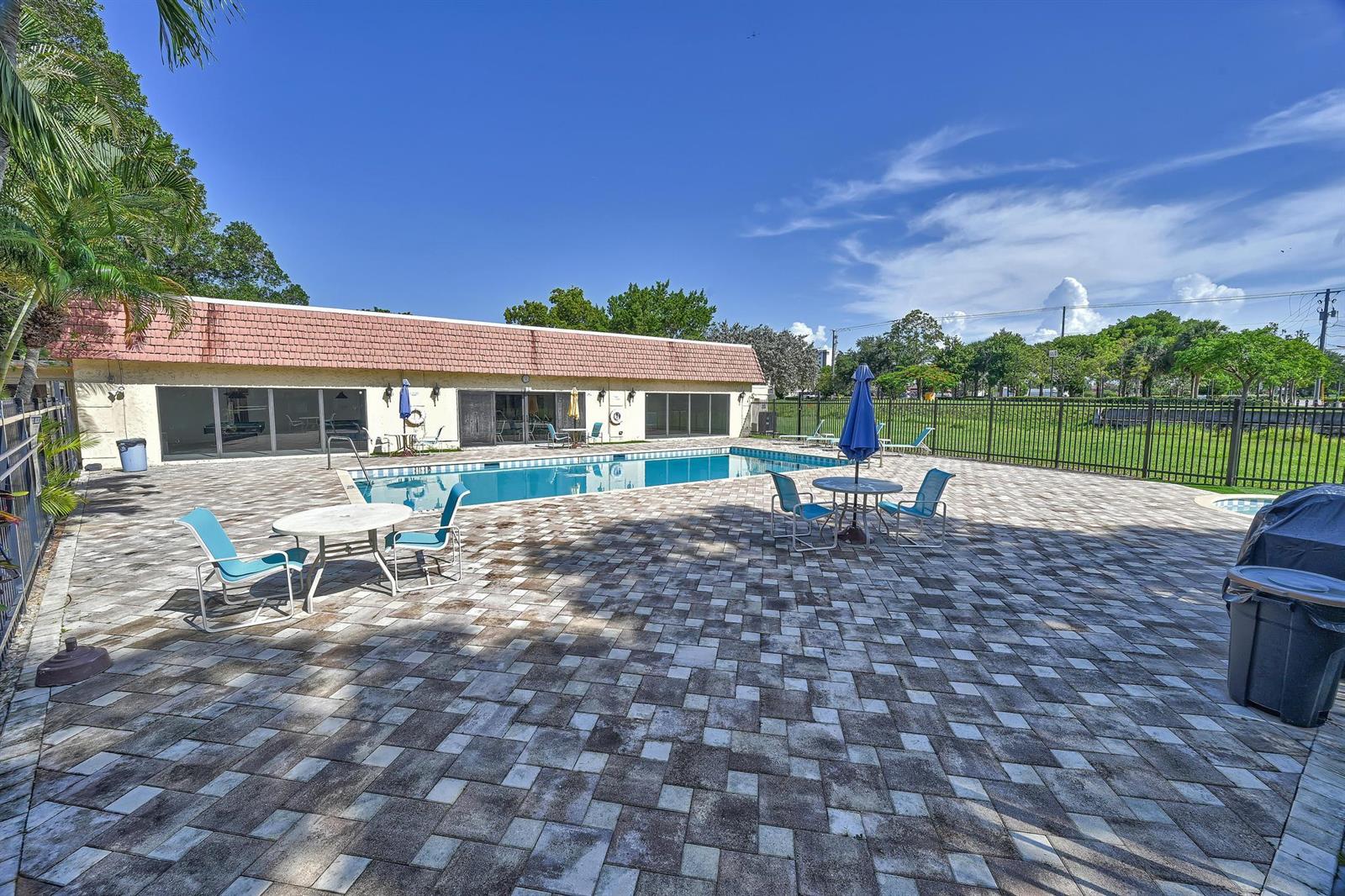 A swimming pool sits on a paved patio in front of a building with glass doors — 134 S Cypress Road # 425, Pompano Beach FL 33060, POMPANO BEACH, FL