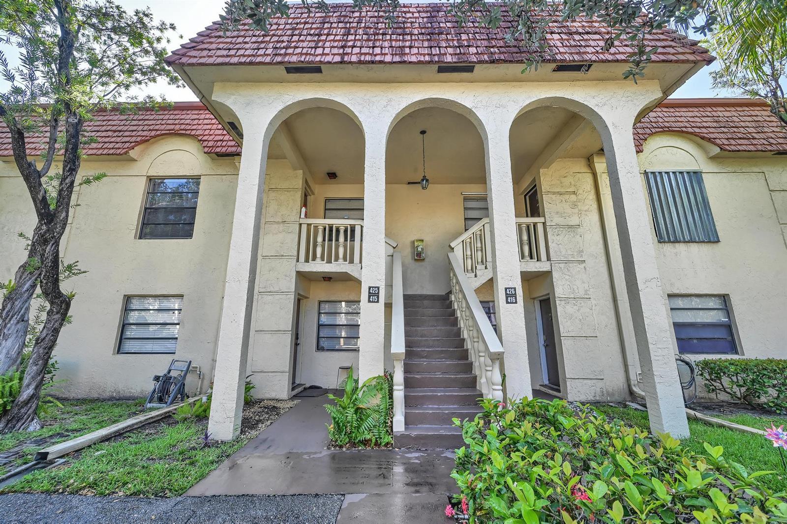 An exterior view of a two-story apartment building with arched entryways and a central staircase — 134 S Cypress Road # 425, Pompano Beach FL 33060, POMPANO BEACH, FL