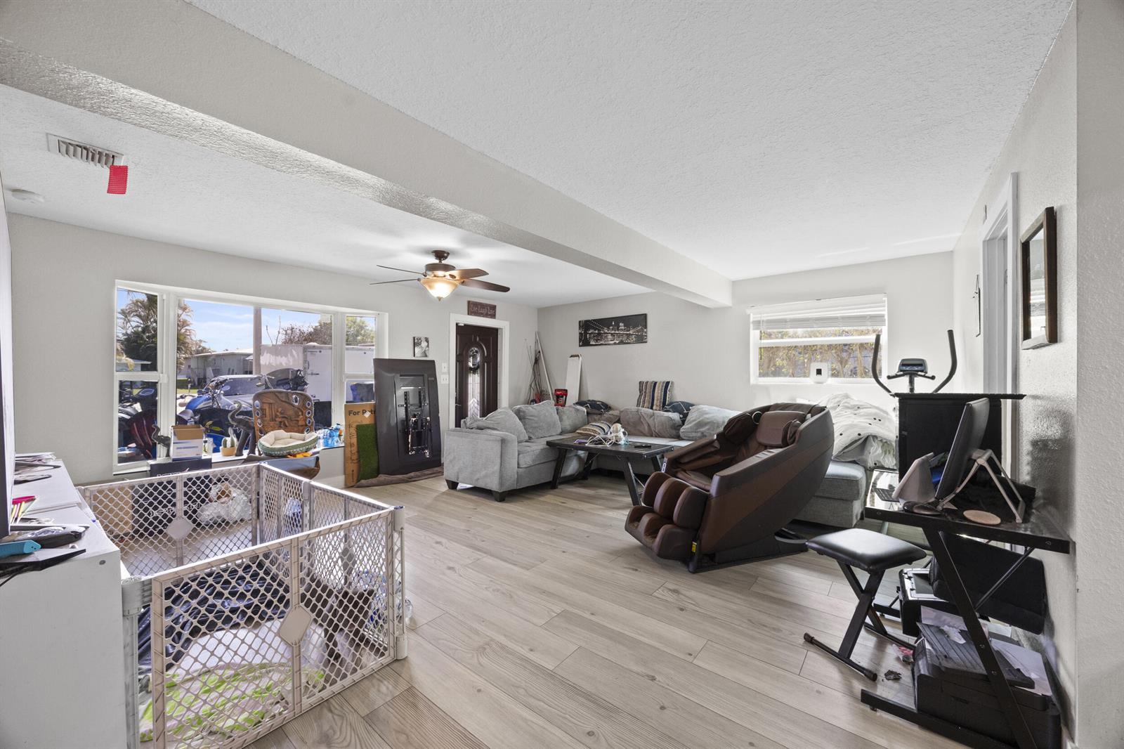A living room features light wood-look flooring, a ceiling fan, a massage chair, and a playpen — 2517 SE Normand Street, Stuart FL 34997, STUART, FL