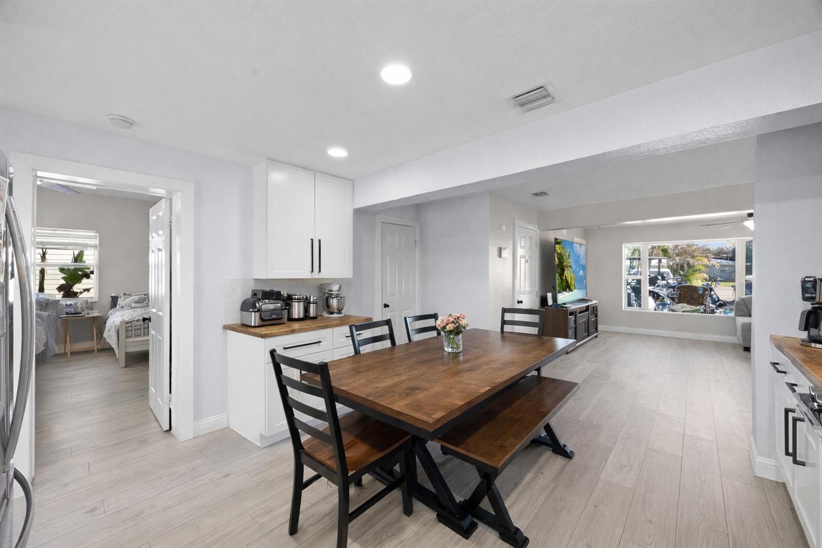 A dining area with a wooden table, chairs, and bench sits near a white kitchen — 2517 SE Normand Street, Stuart FL 34997, STUART, FL