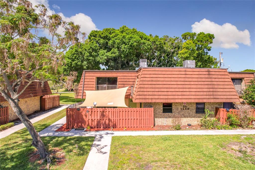 A two-story townhouse with a brown mansard roof, brick facade, and a fenced-in patio area — 1458 N LAWNWOOD CIRCLE UNIT 24A, FORT PIERCE, FL
