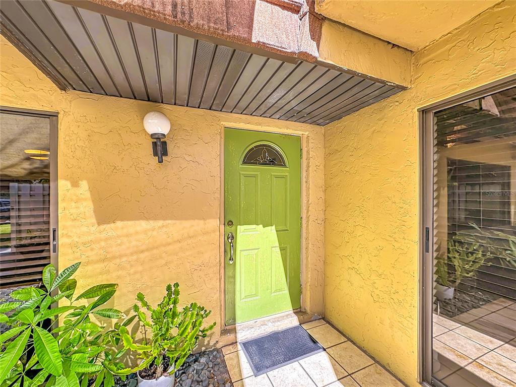 A lime green front door is centered between two sliding glass doors on a patio — 1458 N LAWNWOOD CIRCLE UNIT 24A, FORT PIERCE, FL