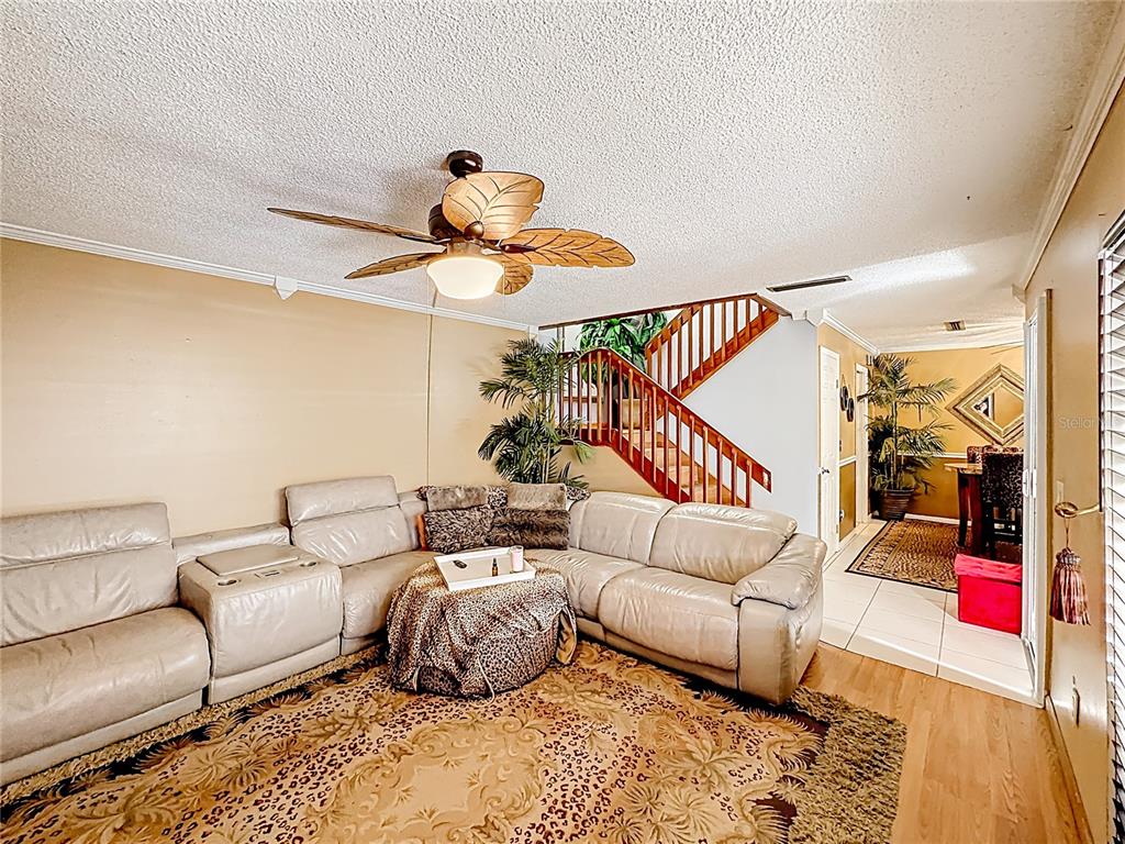 A living room features a large sectional sofa, a leopard-print rug, and a wooden staircase — 1458 N LAWNWOOD CIRCLE UNIT 24A, FORT PIERCE, FL