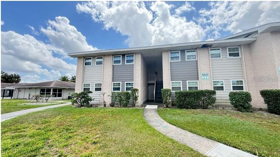 A two-story apartment building with light-colored brick and gray siding under a cloudy sky — 860 SKY LAKE CIRCLE UNIT C412, ORLANDO, FL