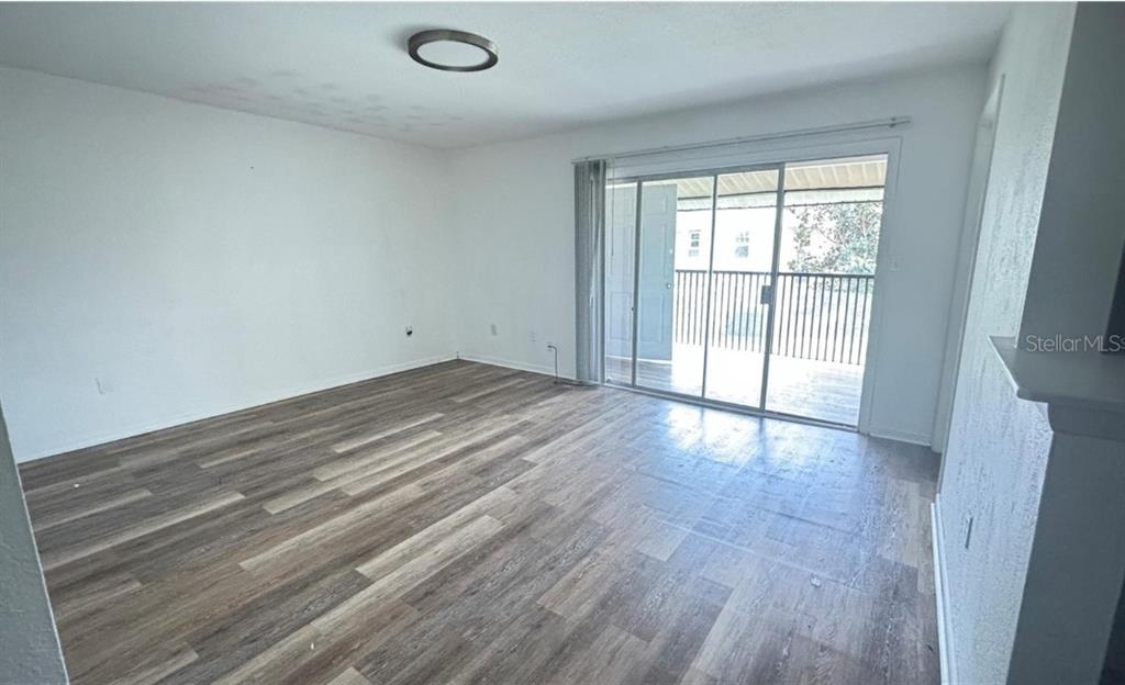 An empty living room features wood-look flooring, white walls, and a sliding glass balcony door — 860 SKY LAKE CIRCLE UNIT C412, ORLANDO, FL