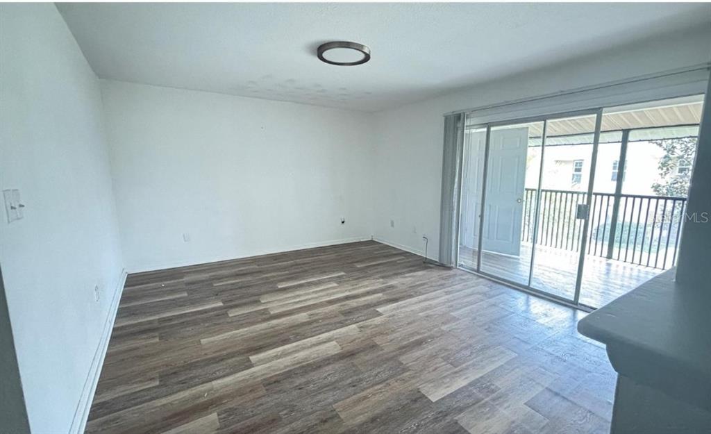 An empty room features wood-look flooring, white walls, a ceiling light, and sliding glass doors — 860 SKY LAKE CIRCLE UNIT C412, ORLANDO, FL