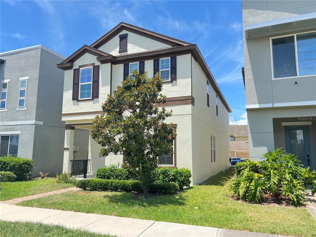 A two-story house with beige stucco siding, brown trim, and a front yard tree — 7867 BERKSHIRE OAK ALLEY, WINDERMERE, FL