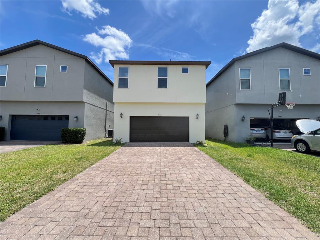 A two-story house with a beige facade and a paved driveway sits between two gray houses — 7867 BERKSHIRE OAK ALLEY, WINDERMERE, FL