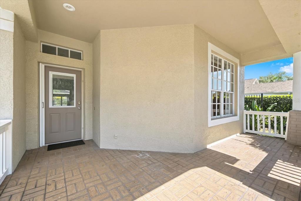A covered front porch features tan stucco walls, a gray door, and brick-patterned pavers — 4628 CORSAGE DRIVE, LUTZ, FL