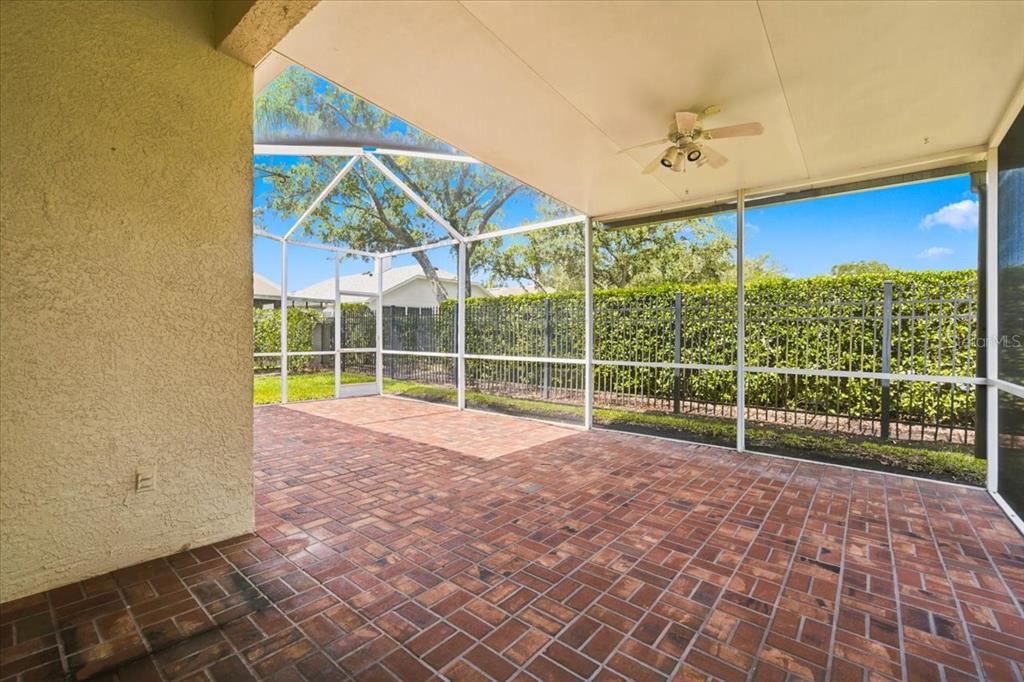 A covered patio with a brick floor and screened-in walls overlooks a fenced backyard — 4628 CORSAGE DRIVE, LUTZ, FL