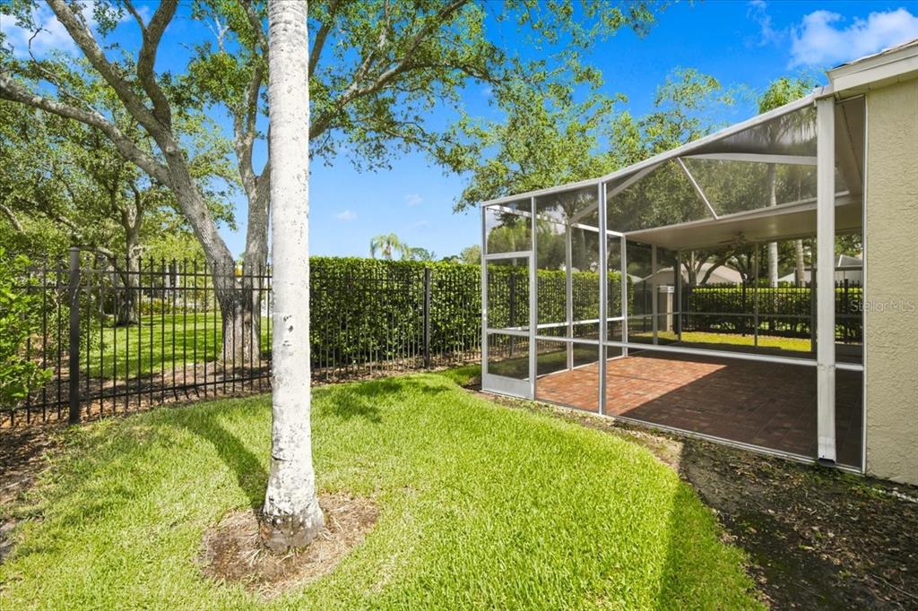 A screened-in patio with brick flooring sits beside a grassy yard and metal fence — 4628 CORSAGE DRIVE, LUTZ, FL
