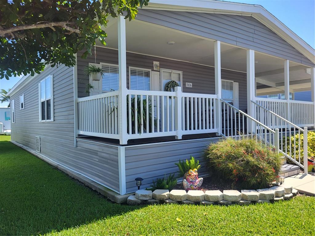 A gray mobile home features a covered front porch with white railings and landscaping — 3106 TERRA SIESTA BOULEVARD, ELLENTON, FL