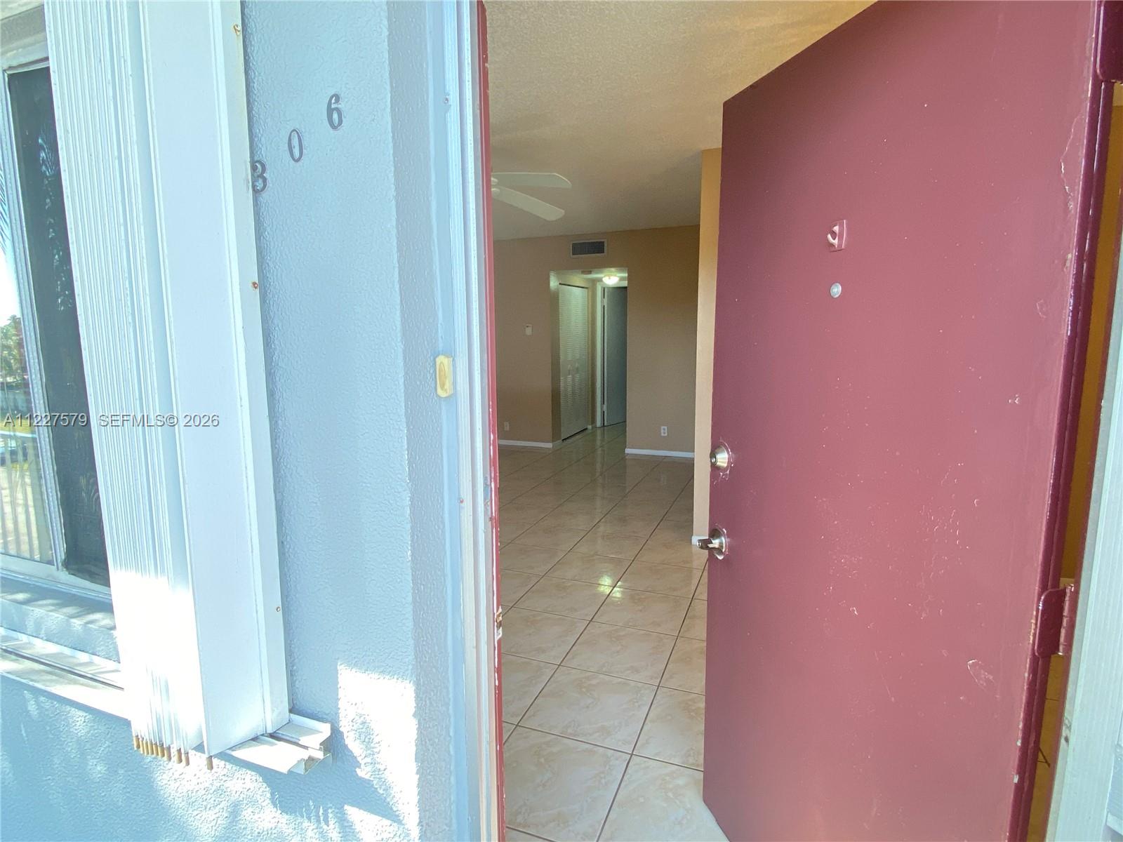 An open red door reveals a tiled interior hallway leading to a living area — 6289 Lear Dr # 306, Lake Worth FL 33462, LAKE WORTH, FL