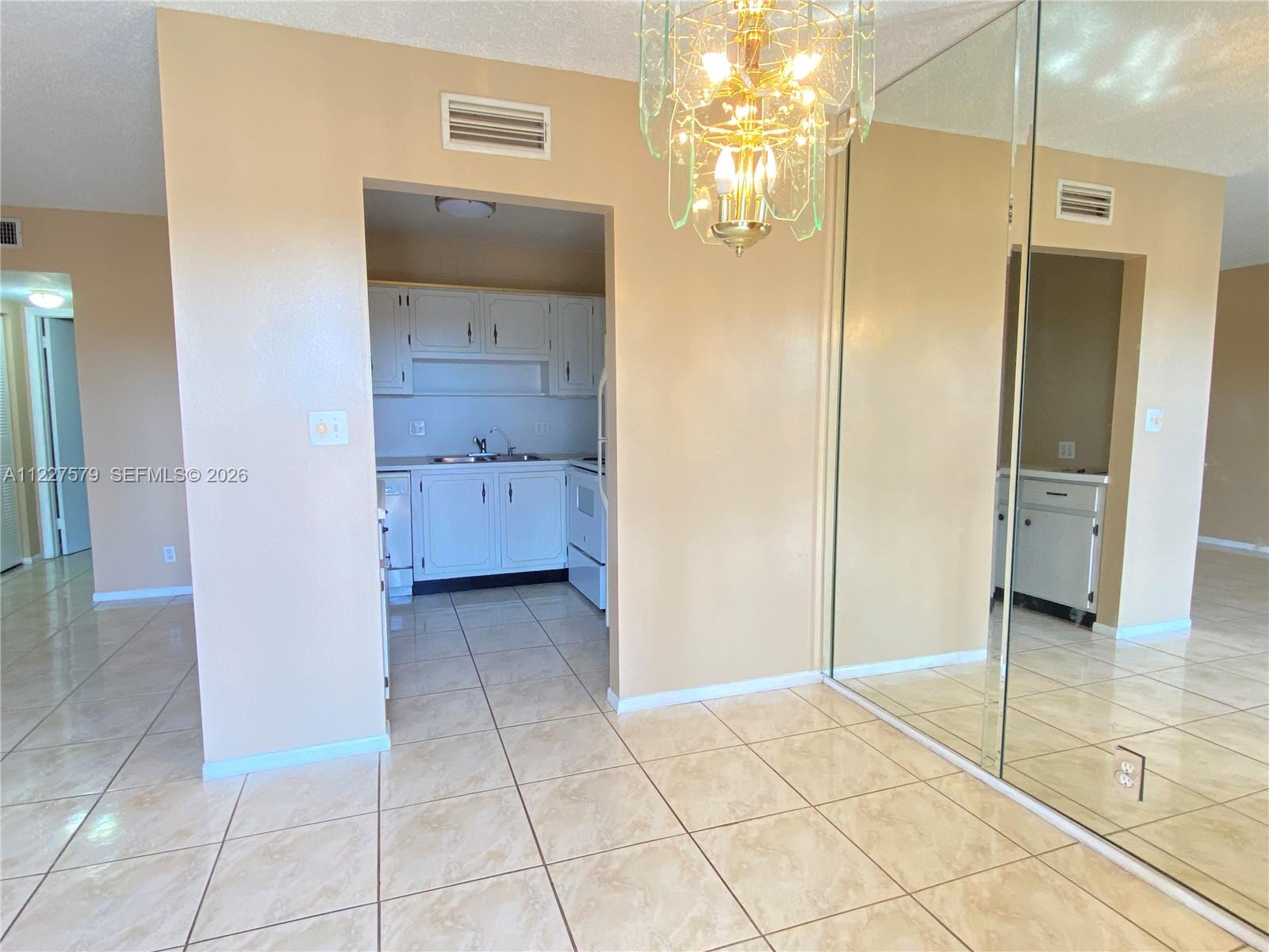 A dining area with a chandelier and mirrored wall leads into a small white kitchen — 6289 Lear Dr # 306, Lake Worth FL 33462, LAKE WORTH, FL