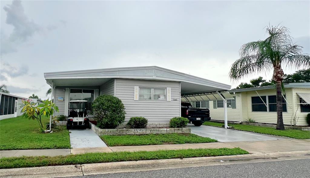A single-story manufactured home with light gray siding, a carport, and a golf cart parked outside — 1100 BELCHER ROAD S UNIT 211, LARGO, FL