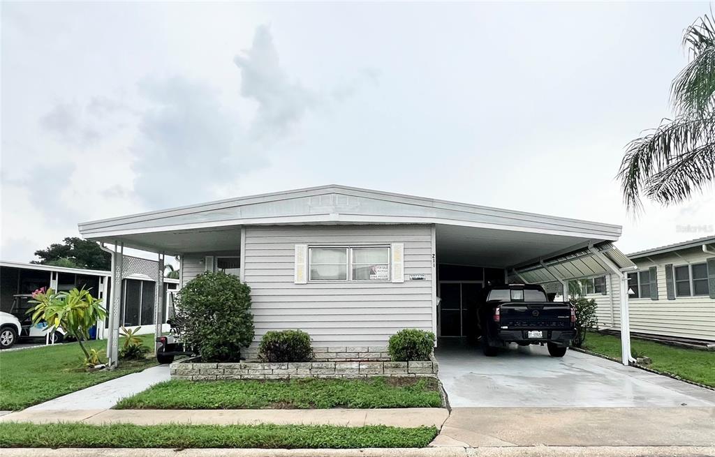 A light gray manufactured home with a carport and a front yard — 1100 BELCHER ROAD S UNIT 211, LARGO, FL