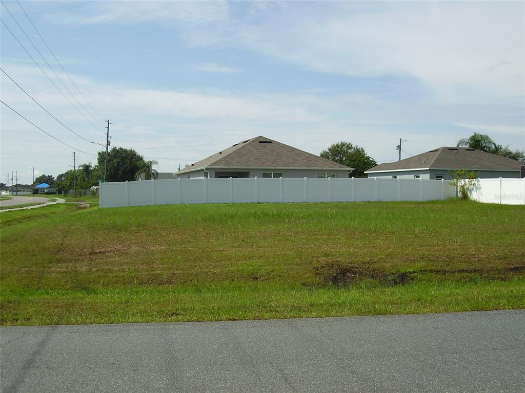 A grassy vacant lot sits in front of a white vinyl fence and suburban houses — 800 CARROUSEL LANE, KISSIMMEE, FL