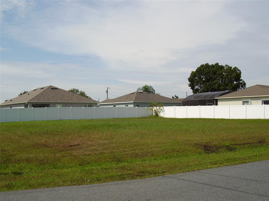 A vacant, grassy residential lot is enclosed by a white vinyl fence near suburban houses — 800 CARROUSEL LANE, KISSIMMEE, FL