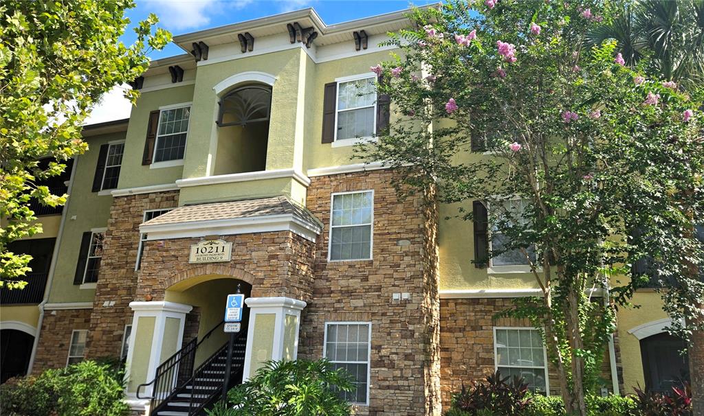 A three-story apartment building exterior features tan stucco walls, stone veneer accents, and a staircase — 10211 COURTNEY PALMS BOULEVARD UNIT 304, TAMPA, FL