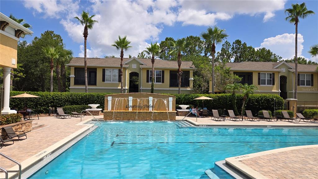 A swimming pool with a stone water feature sits in front of two-story apartment buildings — 10211 COURTNEY PALMS BOULEVARD UNIT 304, TAMPA, FL