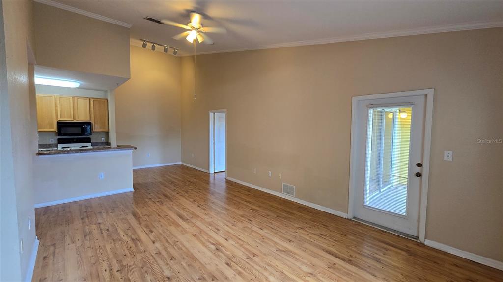 A living room with wood-look flooring, a vaulted ceiling, and an adjacent kitchen area — 10211 COURTNEY PALMS BOULEVARD UNIT 304, TAMPA, FL