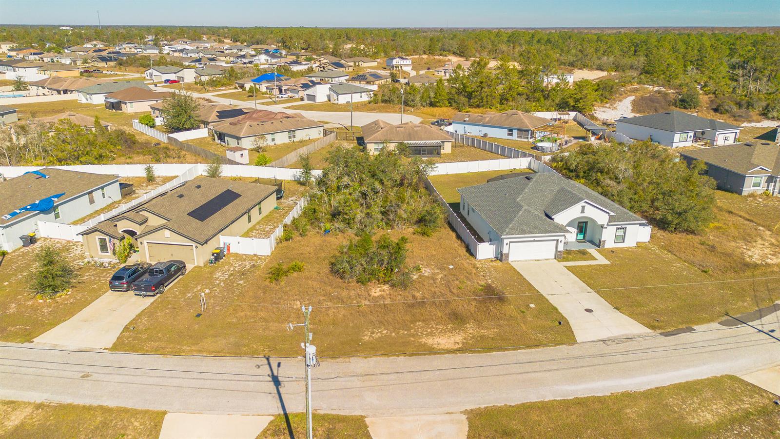 An aerial view shows two suburban houses separated by a vacant, tree-filled lot — 19 Orchid Court, FL 34759, FL