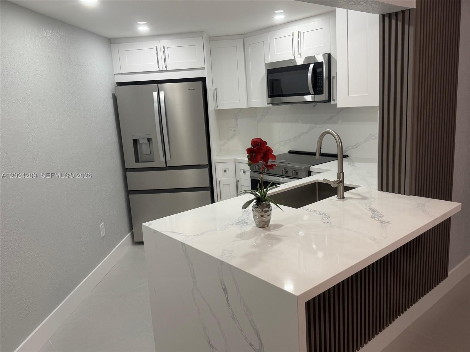A modern kitchen features white cabinets, stainless steel appliances, and a marble-patterned waterfall island — 10233 NW 9th St Cir # 1, Miami FL 33172, MIAMI, FL