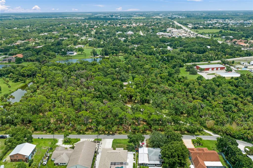 An aerial view shows a residential street bordering a large, wooded lot with a pond — 1210 TWIN LAKES AVENUE, NOKOMIS, FL