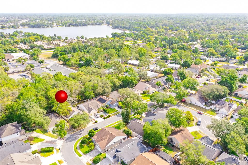An aerial view shows a suburban neighborhood with houses, trees, and a lake in the distance — 254 OAK PARK PLACE, CASSELBERRY, FL