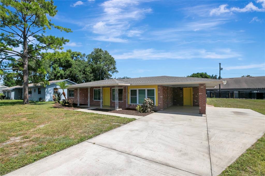 A single-story brick house with a concrete driveway, carport, and two bright yellow doors — 1706 SHORE ACRES DRIVE, LAKELAND, FL