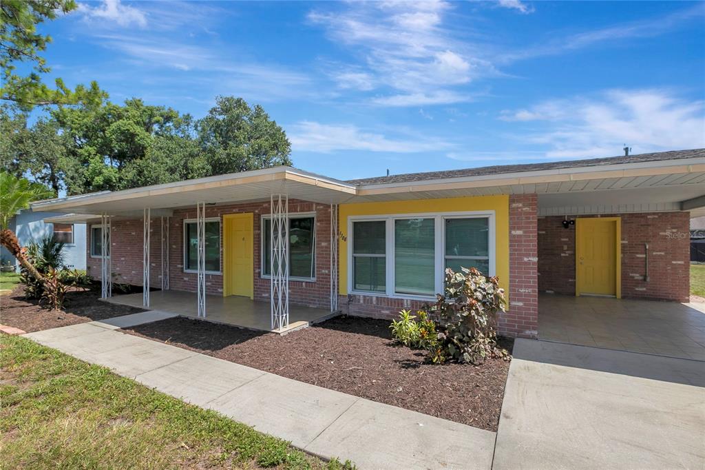 A single-story brick house features a covered porch, yellow doors, and a concrete driveway — 1706 SHORE ACRES DRIVE, LAKELAND, FL