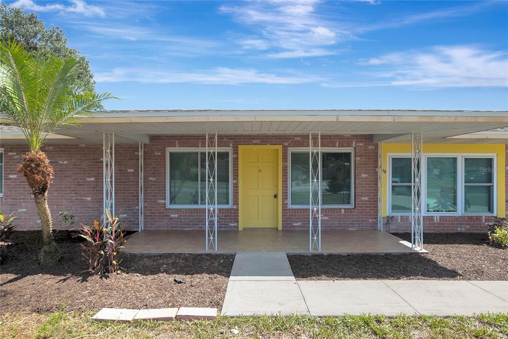 A single-story brick house features a yellow front door, a covered porch, and metal columns — 1706 SHORE ACRES DRIVE, LAKELAND, FL