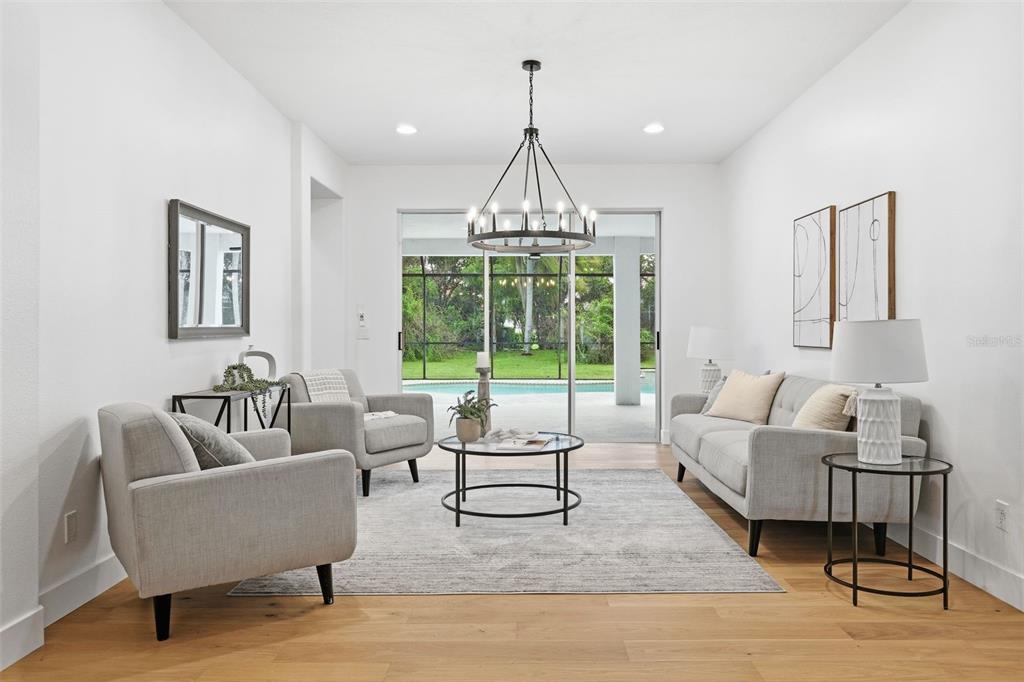 A bright living room features light gray furniture, a round coffee table, and a pool view — 10534 BERMUDA ISLE DRIVE, TAMPA, FL