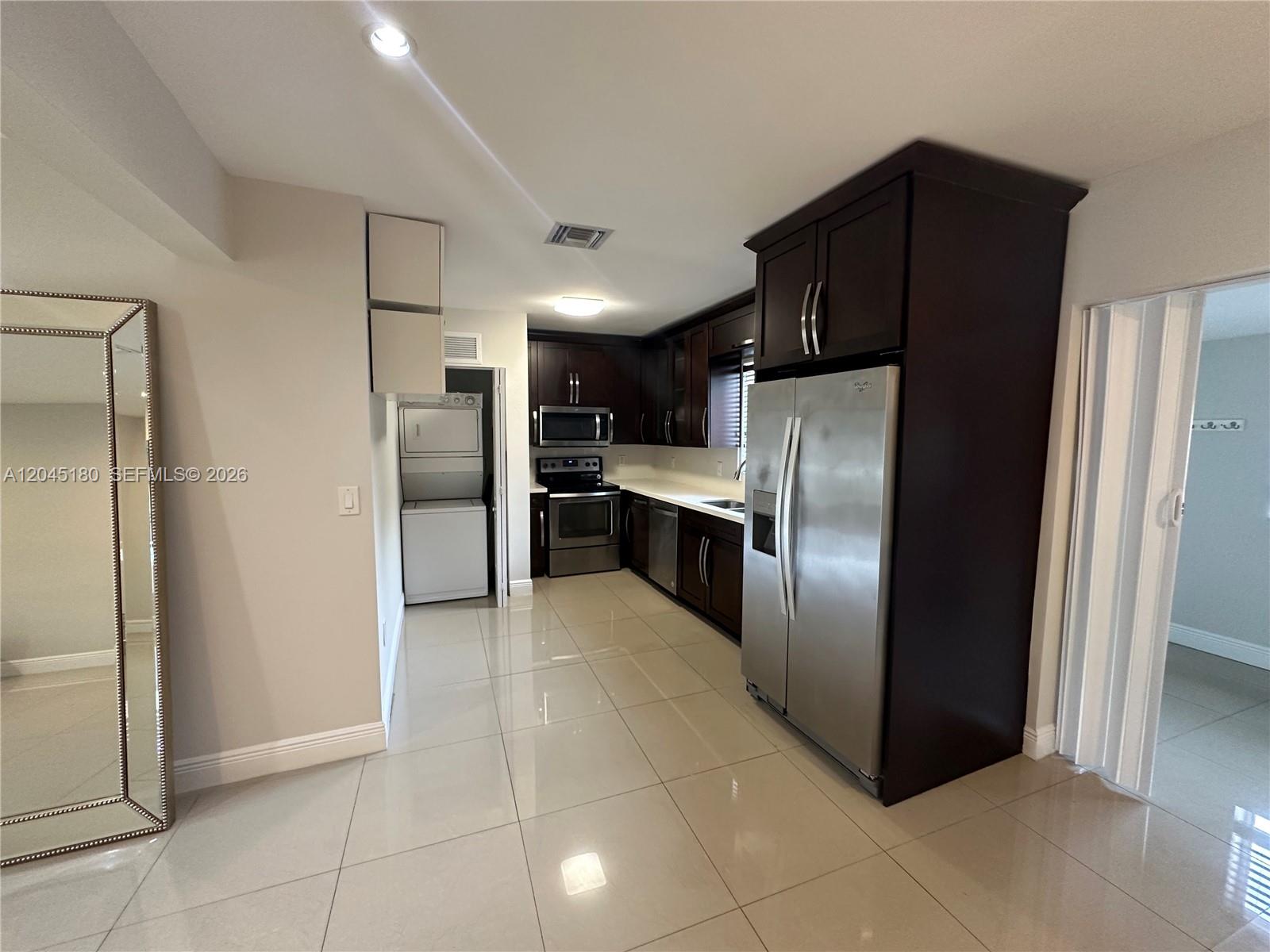 A kitchen features dark wood cabinets, stainless steel appliances, and light-colored tile flooring — 2155 Biarritz Dr, Miami Beach FL 33141, MIAMI BEACH, FL