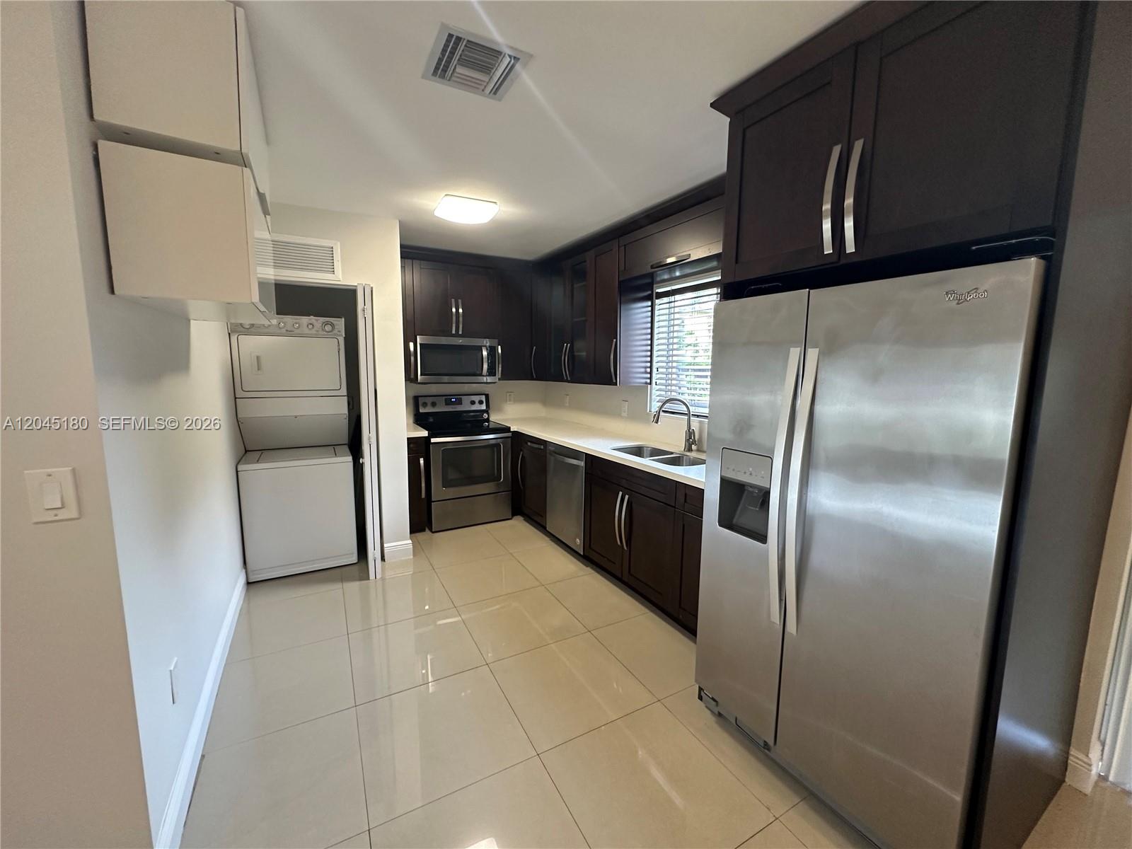 A kitchen features dark wood cabinets, stainless steel appliances, tile flooring, and a laundry closet — 2155 Biarritz Dr, Miami Beach FL 33141, MIAMI BEACH, FL