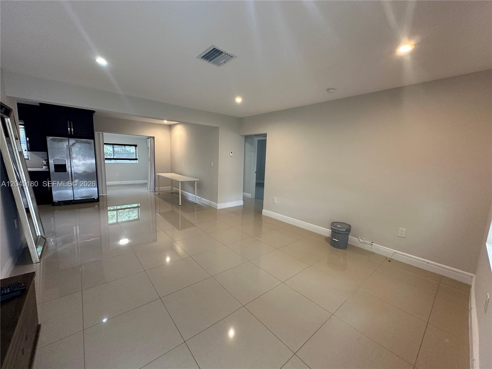 An open-plan living area features large beige floor tiles, recessed lighting, and a kitchen — 2155 Biarritz Dr, Miami Beach FL 33141, MIAMI BEACH, FL