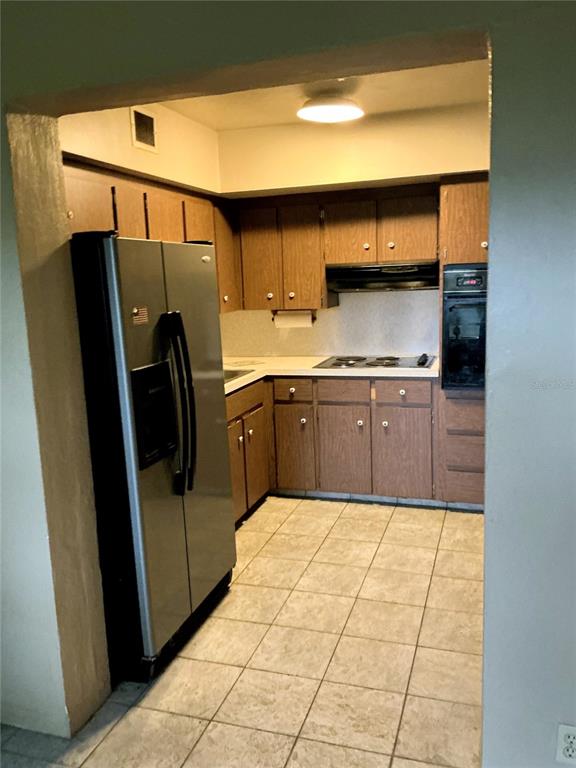 A kitchen features wood cabinets, a stainless steel refrigerator, a cooktop, and tiled flooring — 4300 58TH STREET N UNIT 1801, KENNETH CITY, FL
