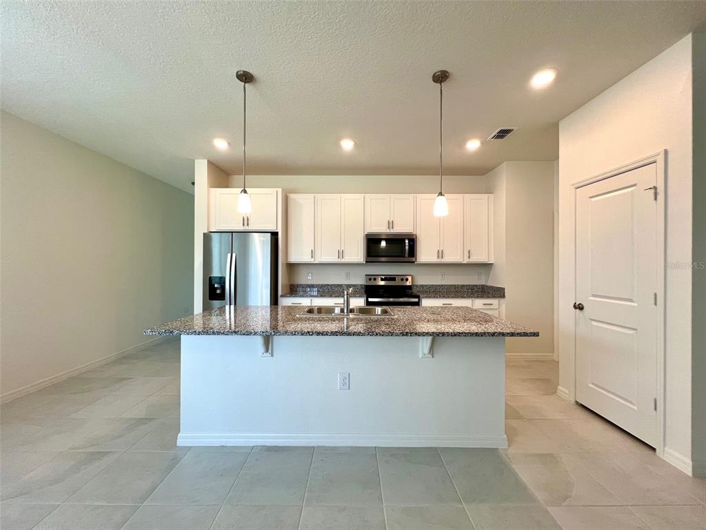 A kitchen features white cabinets, granite countertops, a center island, and stainless steel appliances — 16365 WINDING PRESERVE CIRCLE, CLERMONT, FL