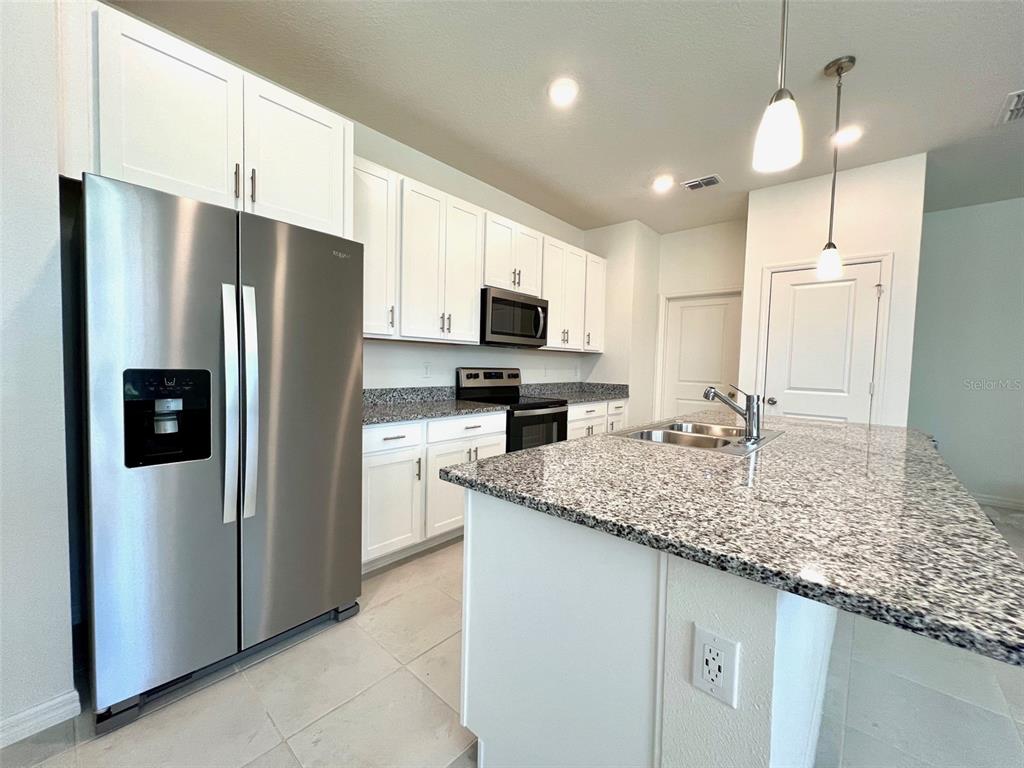 A kitchen features white cabinets, stainless steel appliances, and a granite-topped island — 16365 WINDING PRESERVE CIRCLE, CLERMONT, FL
