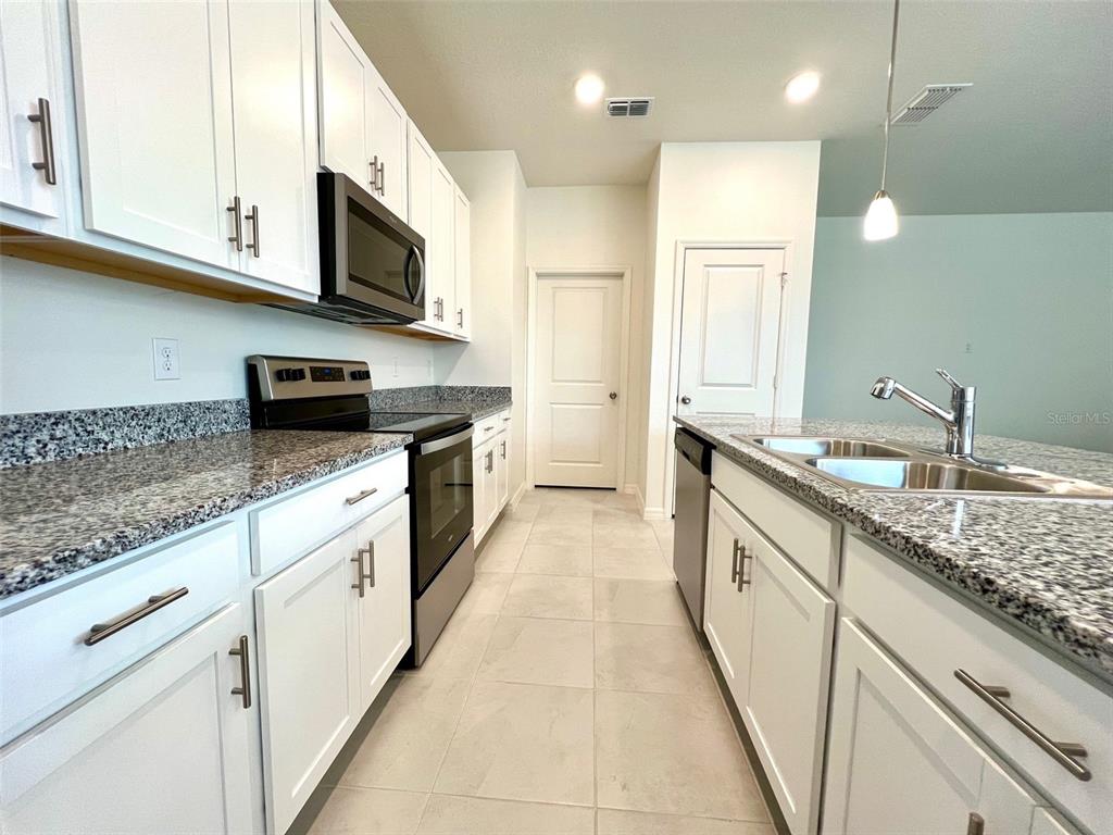 A kitchen features white cabinets, granite countertops, stainless steel appliances, and tile flooring — 16365 WINDING PRESERVE CIRCLE, CLERMONT, FL