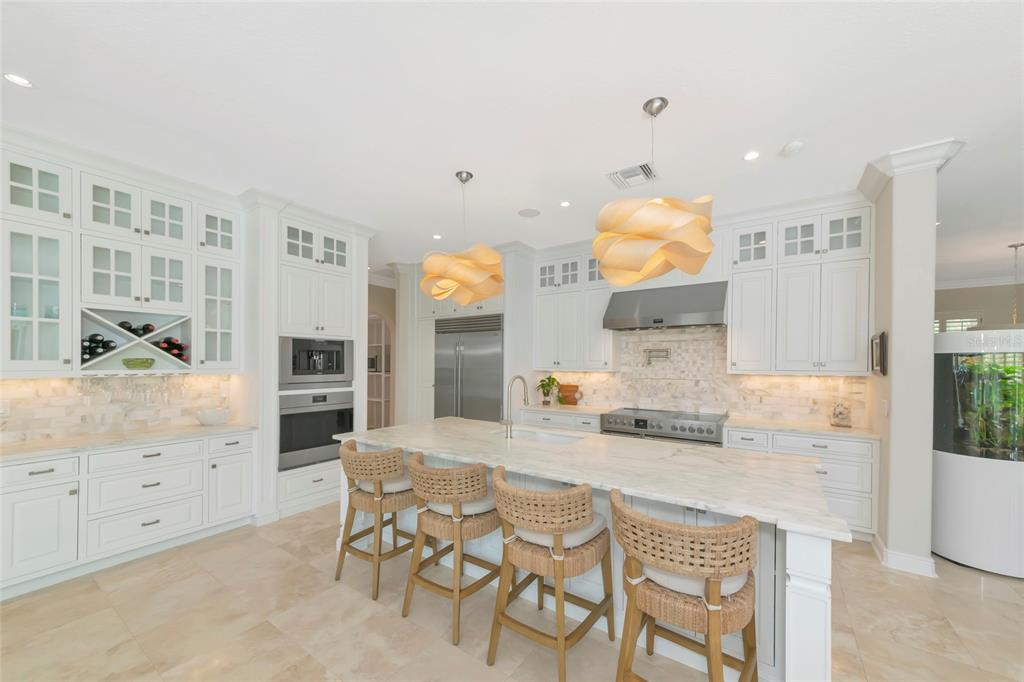 A white kitchen features a marble island, woven bar stools, and two sculptural pendant lights — 7631 COVE TERRACE, SARASOTA, FL
