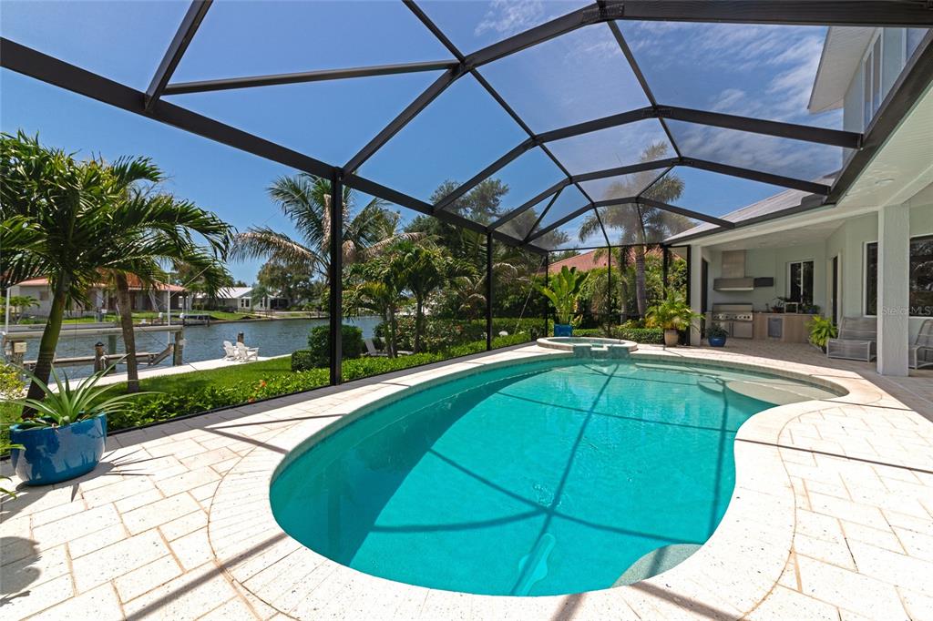 A screened-in pool and spa area overlooks a canal with palm trees and landscaping — 7631 COVE TERRACE, SARASOTA, FL