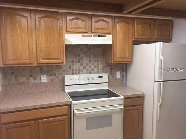 A kitchen features oak cabinets, a white stove, a tiled backsplash, and a white refrigerator — 2621 COVE CAY DRIVE UNIT 105, CLEARWATER, FL