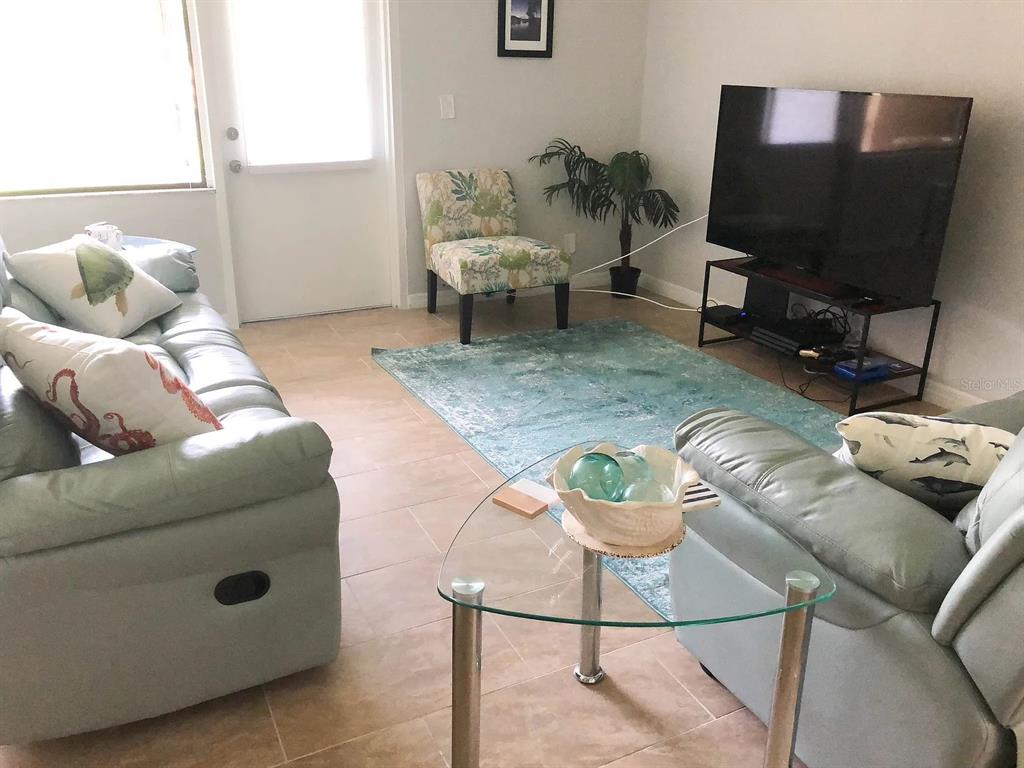 A living room features light-colored tile floors, a blue area rug, and light blue furniture — 2621 COVE CAY DRIVE UNIT 105, CLEARWATER, FL