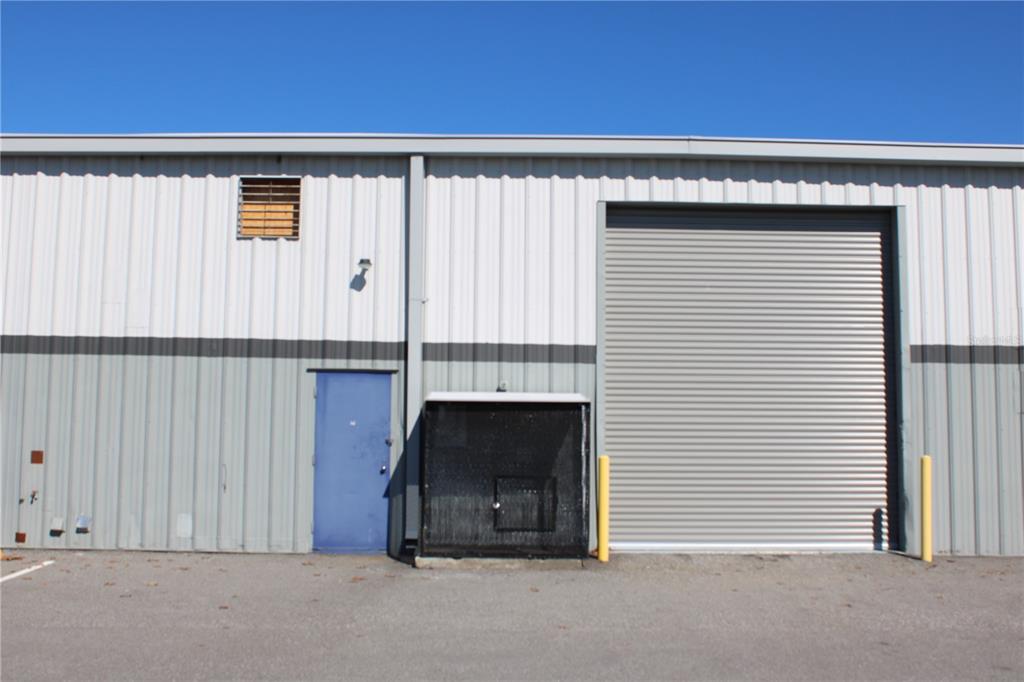 The exterior of a metal warehouse building features a blue door and a roll-up door — 1400 L AND R INDUSTRIAL BOULEVARD Bldg. A, TARPON SPRINGS, FL