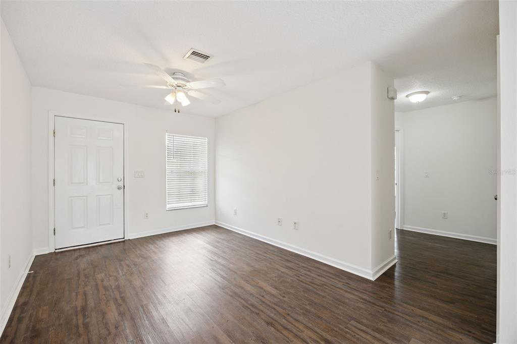 An empty room with white walls, dark wood-look flooring, a ceiling fan, and a front door — 1105 N ROCKINGHAM AVENUE, TAVARES, FL