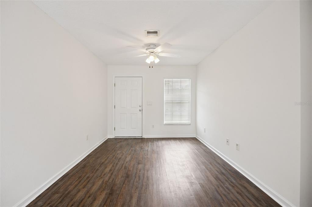 An empty room with white walls, dark wood-look flooring, a ceiling fan, and a door — 1105 N ROCKINGHAM AVENUE, TAVARES, FL